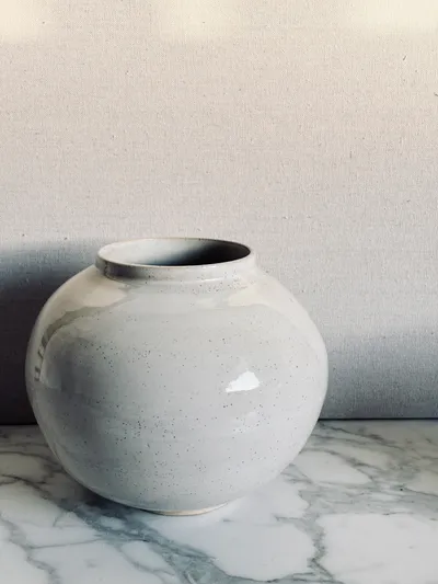 A speckled white moon jar on a marble surface