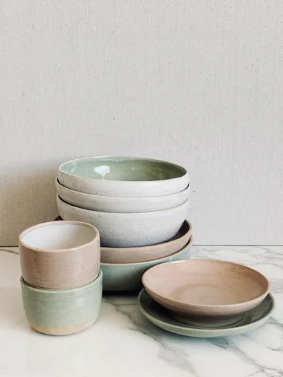 A stack of bowls and cups in celadon and blush glazes