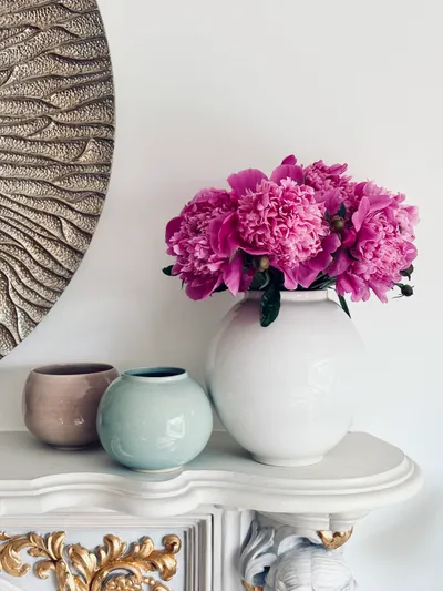 A white moon jar holding pink peonies, with a celadon cup alongside