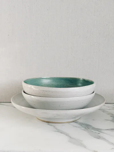 Two speckled bowls, one glazed teal inside, stacked on a plate