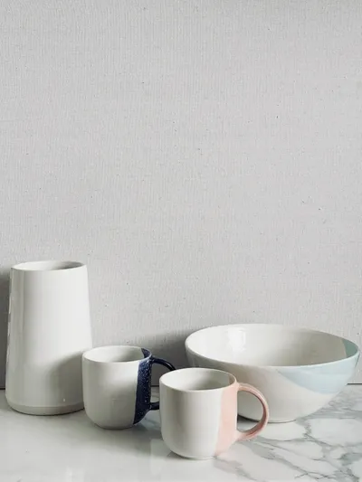 A white cylinder vase with two handled mugs and a shallow bowl