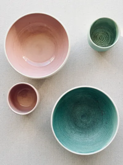 A flat lay of bowls and cups in pink and teal glazes on linen